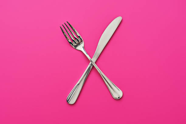 Dont eat too much. Knife and fork crossed, isolated on pink background