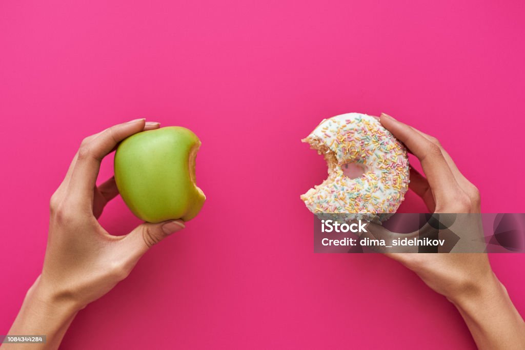 Dieting or good health concept. Young woman trying to choose between apple and donut Dieting or good health concept. Young woman rejecting Junk food or unhealthy food such as donut or dessert and choosing healthy food such as fresh fruit or vegetable. Healthy Eating Stock Photo