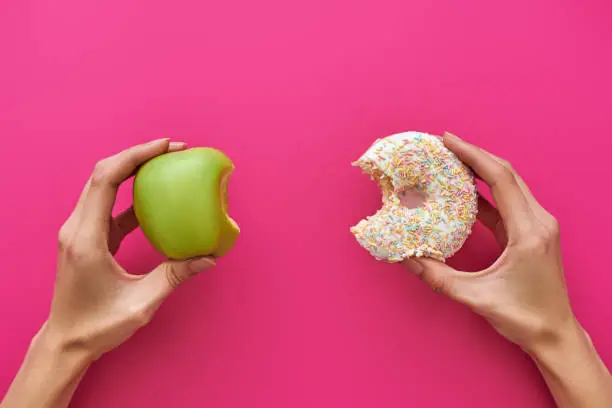 Photo of Dieting or good health concept. Young woman trying to choose between apple and donut