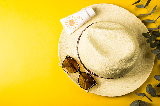 Beach accessories. Summer hat, sunglasses and suntan lotion on a yellow background