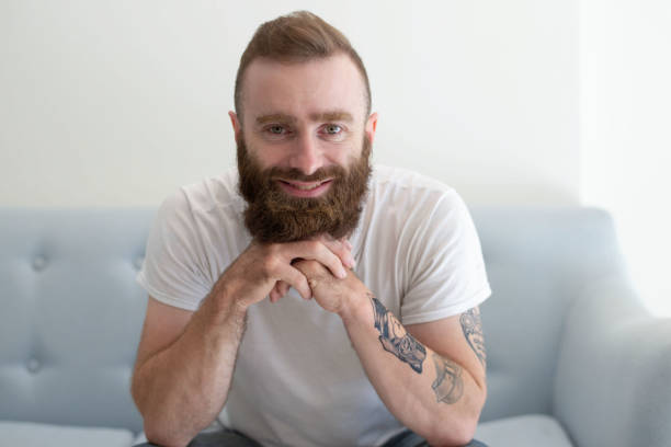 istock Cheerful bearded young man with tattoo sitting on couch 1084353880