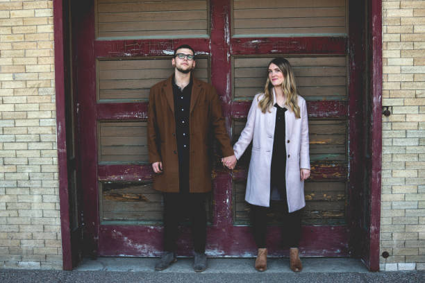 lindo largo humorístico retrato de una pareja hipster posando delante de una antigua puerta de garaje - couple old fashioned hipster holding hands fotografías e imágenes de stock