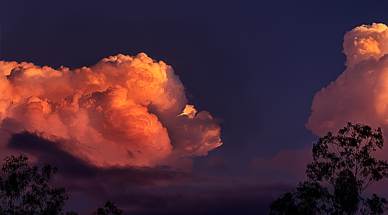 Orange glow of massive thunderstorm clouds approaching at sunset in a landscape panoramic view