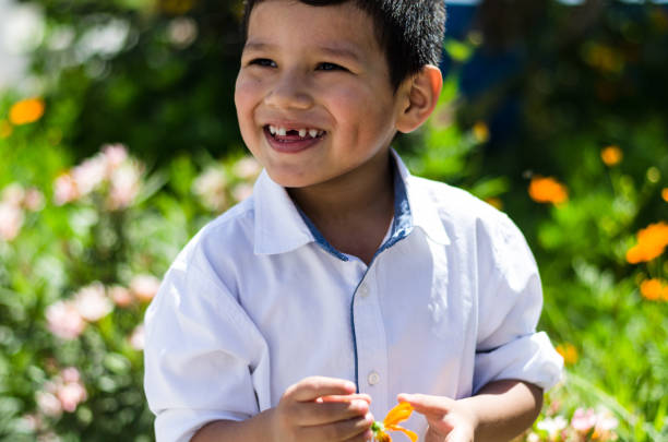 small baby boy holding a daisy in his hand and laughing in the field of flowers