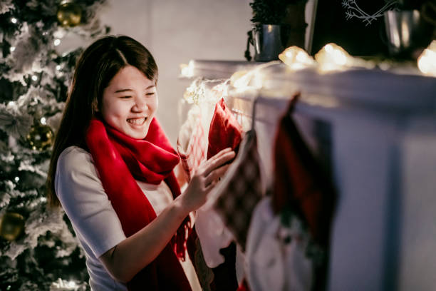 an asian chinese female decorating at home hanging Christmas stocking an asian chinese female decorating at home hanging Christmas stocking asian women in stockings stock pictures, royalty-free photos & images