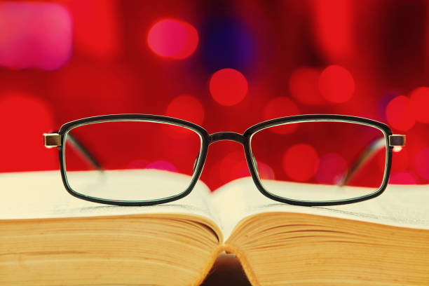 The hands of an old man hold an open book and glasses