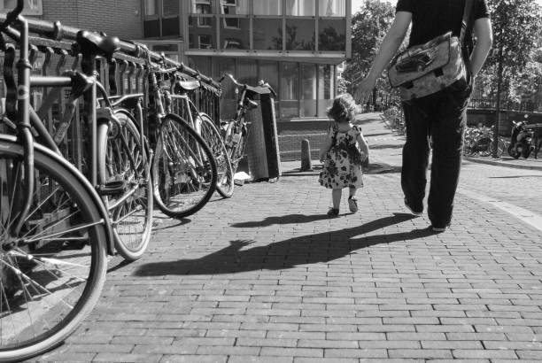 Walk safely, little girl Amsterdam, Netherlands - 2012-09-09: Photo of a young father guiding and protecting his little girl in her first steps - Veilige wandeling, kleintje - Fietsen in Amsterdam serie. Bicycles in Amsterdam series. Amsterdam Street Photography. Editorial jordaan amsterdam stock pictures, royalty-free photos & images