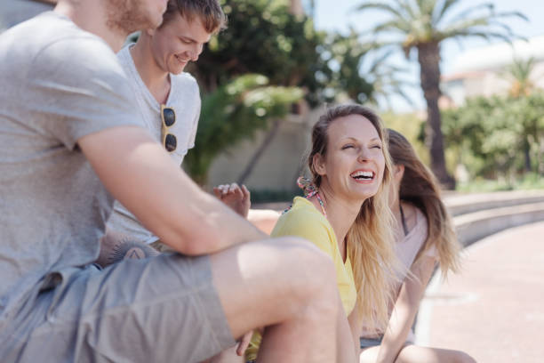 Laughing young woman with her friends sitting on steps on a pedestrian promenade relaxing in the shade of a tree