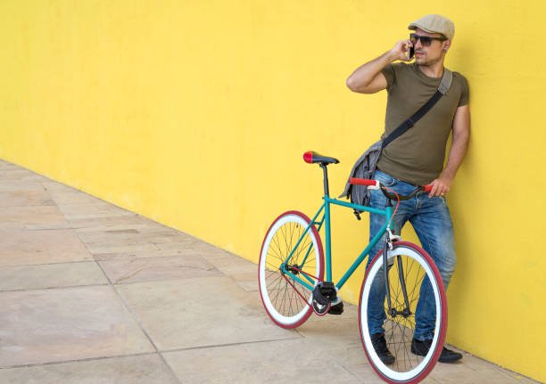 istock Man talking on smart phone while standing by bicycle against yellow wall at sidewalk in city 1084438638