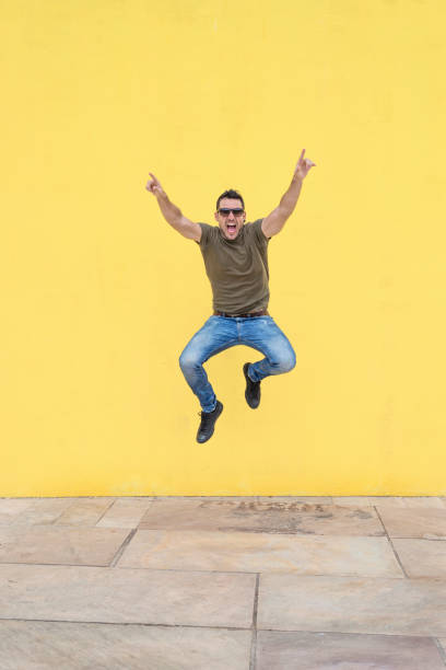 istock Young man with sunglasses jumping against a yellow wall. 1084440046