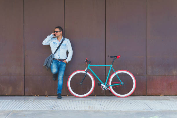 istock Man talking on smart phone while standing by bicycle against metallic wall at sidewalk in city 1084440060
