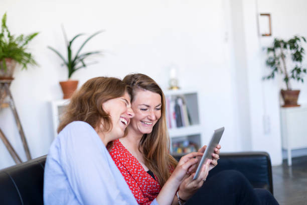 istock Two beautiful young women at home sitting on sofa while using a tablet PC computer and smiling 1084440502