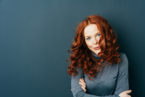 Portrait of young beautiful red-haired woman against dark background with copy space