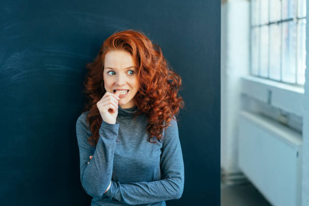 Worried young woman biting her nail in trepidation stock photo