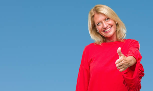 istock Middle age blonde woman over isolated background smiling friendly offering handshake as greeting and welcoming. Successful business. 1084451444
