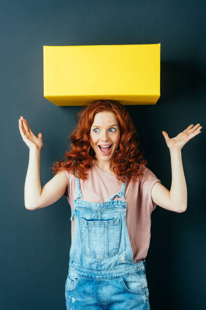 istock Young cheerful woman with yellow box on her head 1084451654