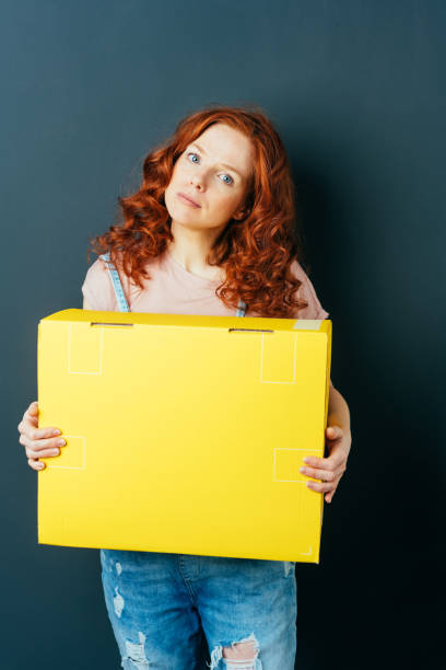 istock Young red-haired woman holding yellow box 1084451656
