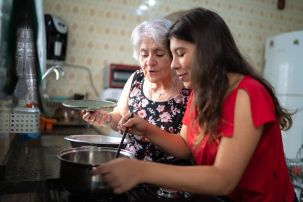 grandmother teaching her granddaughter how to cook - cozinhar imagens e fotografias de stock