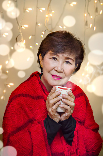 Portrait of old woman holding hot coffee cup with the light of the bokeh on background