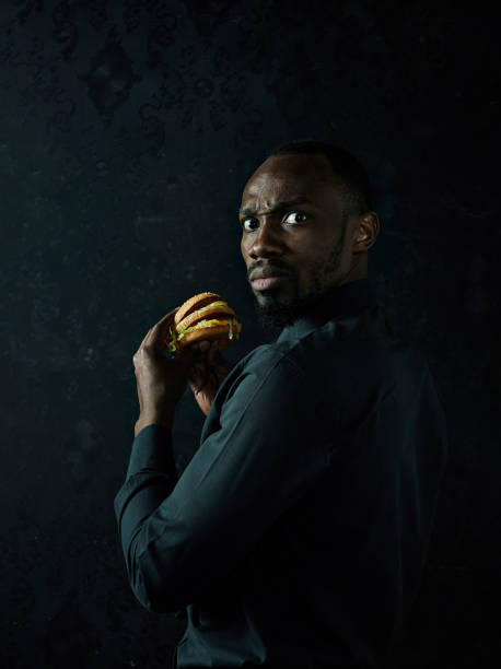 istock young african american man eating hamburger and looking away on black studio 1084464504
