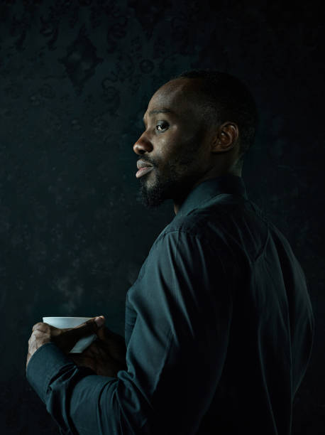 istock Stylish young black man with cup of coffee posing on dark background. 1084464542
