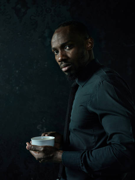 istock Stylish young black man with cup of coffee posing on dark background. 1084464554