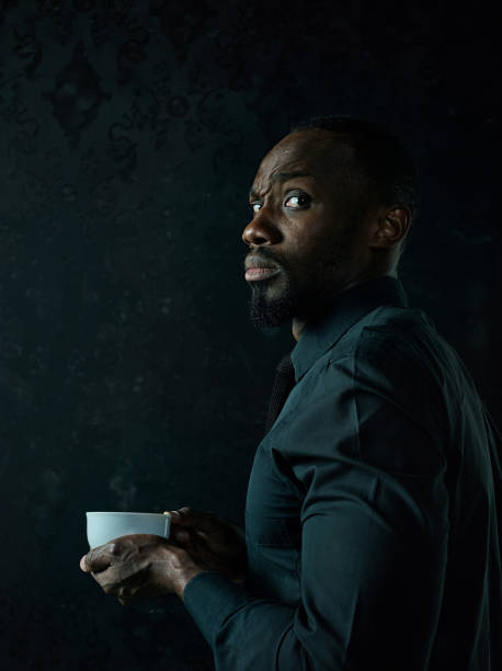 istock Stylish young black man with cup of coffee posing on dark background. 1084464574