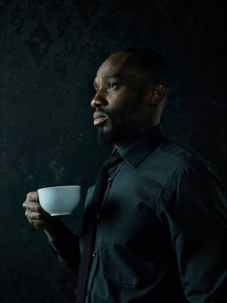 istock Stylish young black man with cup of coffee posing on dark background. 1084464586