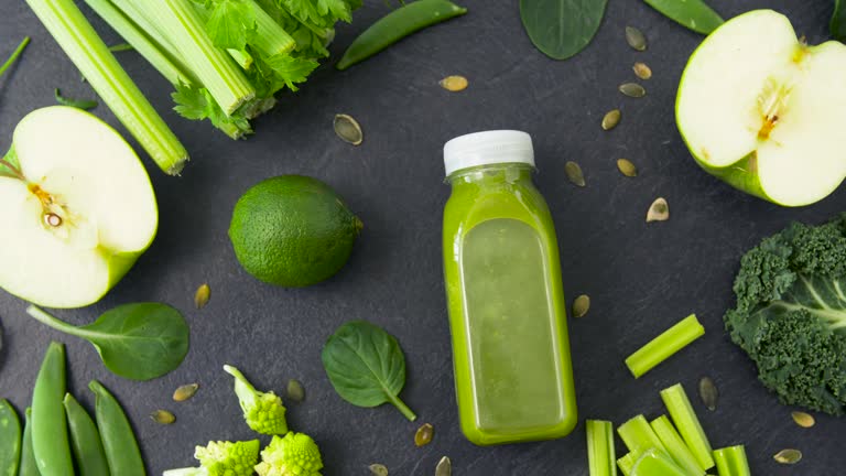 bottle with green juice and vegetables on table