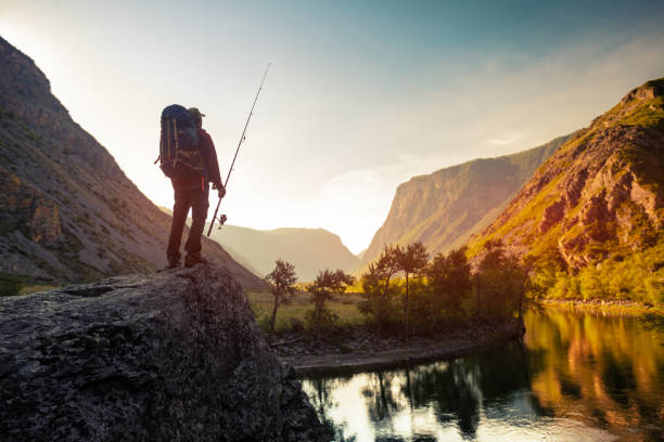 Hiker stands on the rock Hiker stands on the rock with backpack and fishing rod and enjoys sunrise river view altai nature reserve photos stock pictures, royalty-free photos & images