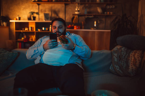 istock Lazy chubby man sitting on sofa and using smart phone 1084478930