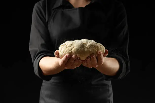 The chef holds the dough for bread, pizza, sweets. On a black background. Close-up,Food concept.