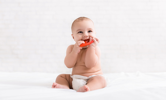 Infant growing first tooth. Cute newborn baby biting teether in bed, copy space