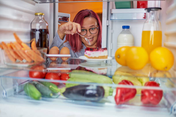 istock Woman eating cake while standing in front of fridge. 1084488040