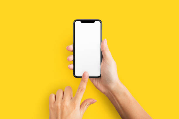 Mockup of female hand holding cell phone with blank screen Mockup of female hands touching cell phone with blank screen on yellow background. web page photos stock pictures, royalty-free photos & images