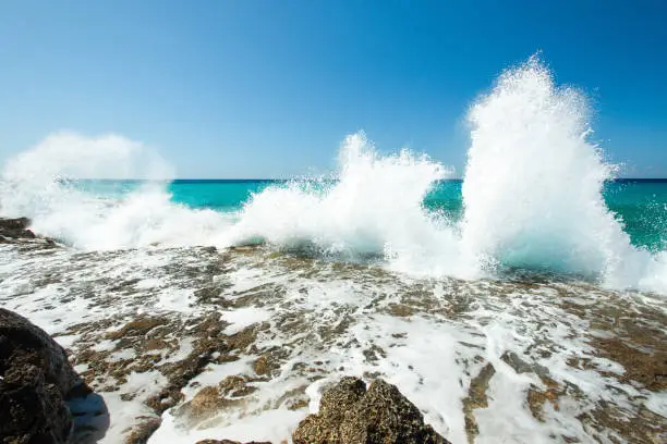 High waves of the Caribbean Sea are splashing hardly against rocks on a coastline at hot summer sunny day