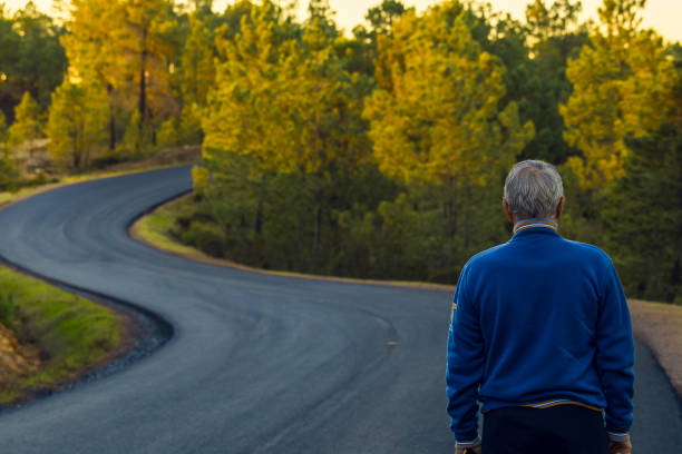 Active senior man of back walking on lonely highway for the mountains Active senior man stands alone on lonely road between mountains. Older man of back walking on lonely highway personal perspective standing stock pictures, royalty-free photos & images