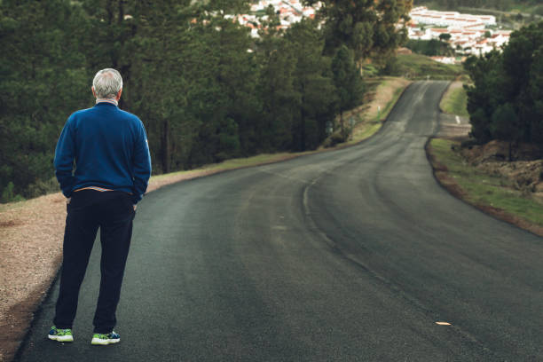 Active senior man standing on lonely road between mountains Active senior man standing on lonely road between mountains. Older man of back standing on lonely highway person falling backwards stock pictures, royalty-free photos & images