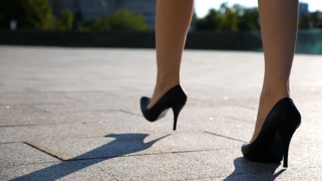 Female legs in high heels shoes walking in the urban street. Feet of young business woman in high-heeled footwear going in the city. Girl stepping to work. Slow motion Close up Low angle view
