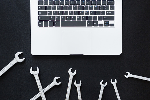 Laptop and wrench on black background, top view, flat lay