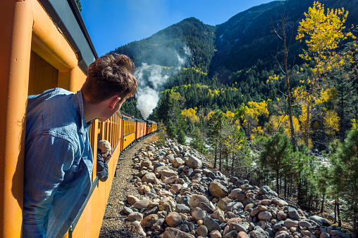 Young man looking out of train window on the historic steam engine train travelling from Durango to Silverton along the Animas River in Colorado, USA.