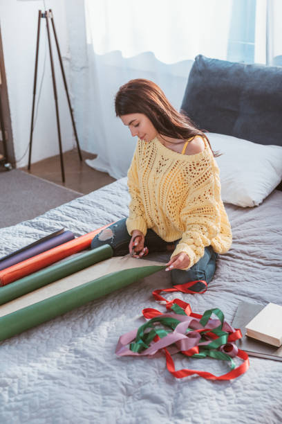 istock attractive girl packing christmas gift while sitting on bed at home 1084543096