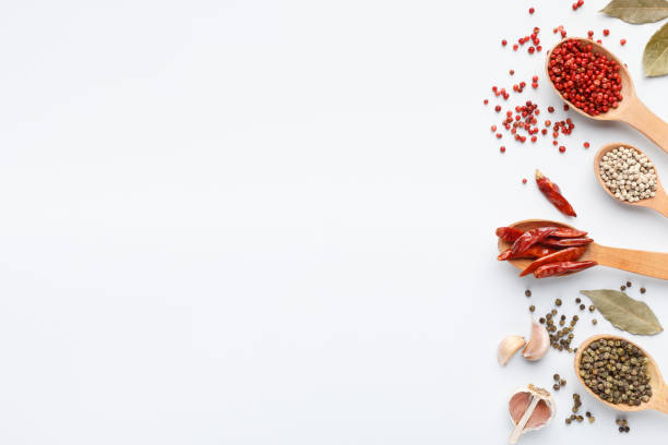 Various peppercorns in spoons on white background