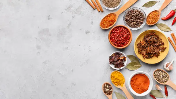 Colorful spices in spoons and bowls with fresh seasoning on grey background, top view, copy space