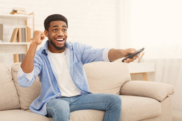 istock Young african-american man watching TV at home 1084560490