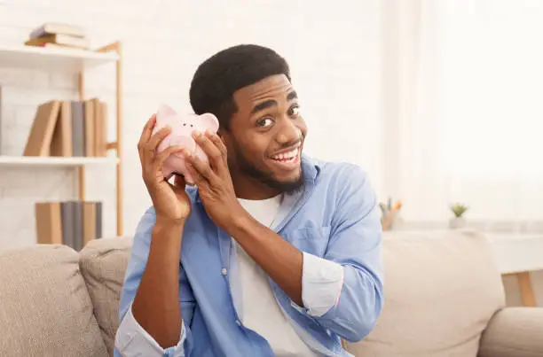 Photo of Happy black man with piggybank at home