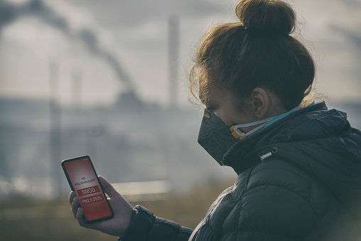 Mujer con una máscara de cara real contra la contaminación y control de contaminación del aire actual con aplicación de teléfono inteligente photo