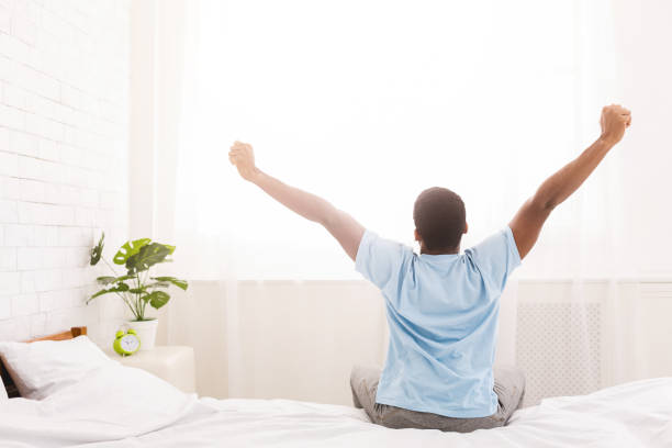 istock Young man waking up in bed and stretching his arms 1084565872