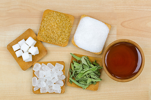 Sugar cubes, brown sugar crystals, granulated white sugar, rock sugar, stevia, honey, Different types of sweetness, top view on wooden background