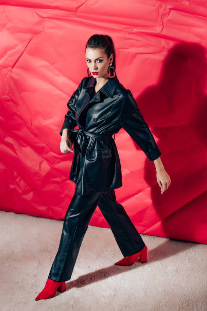istock beautiful model posing in black leather suit on red background 1084571678